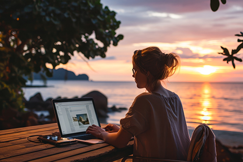 Mujer trabajando en su laptop al aire libre, junto al mar, durante el atardecer.